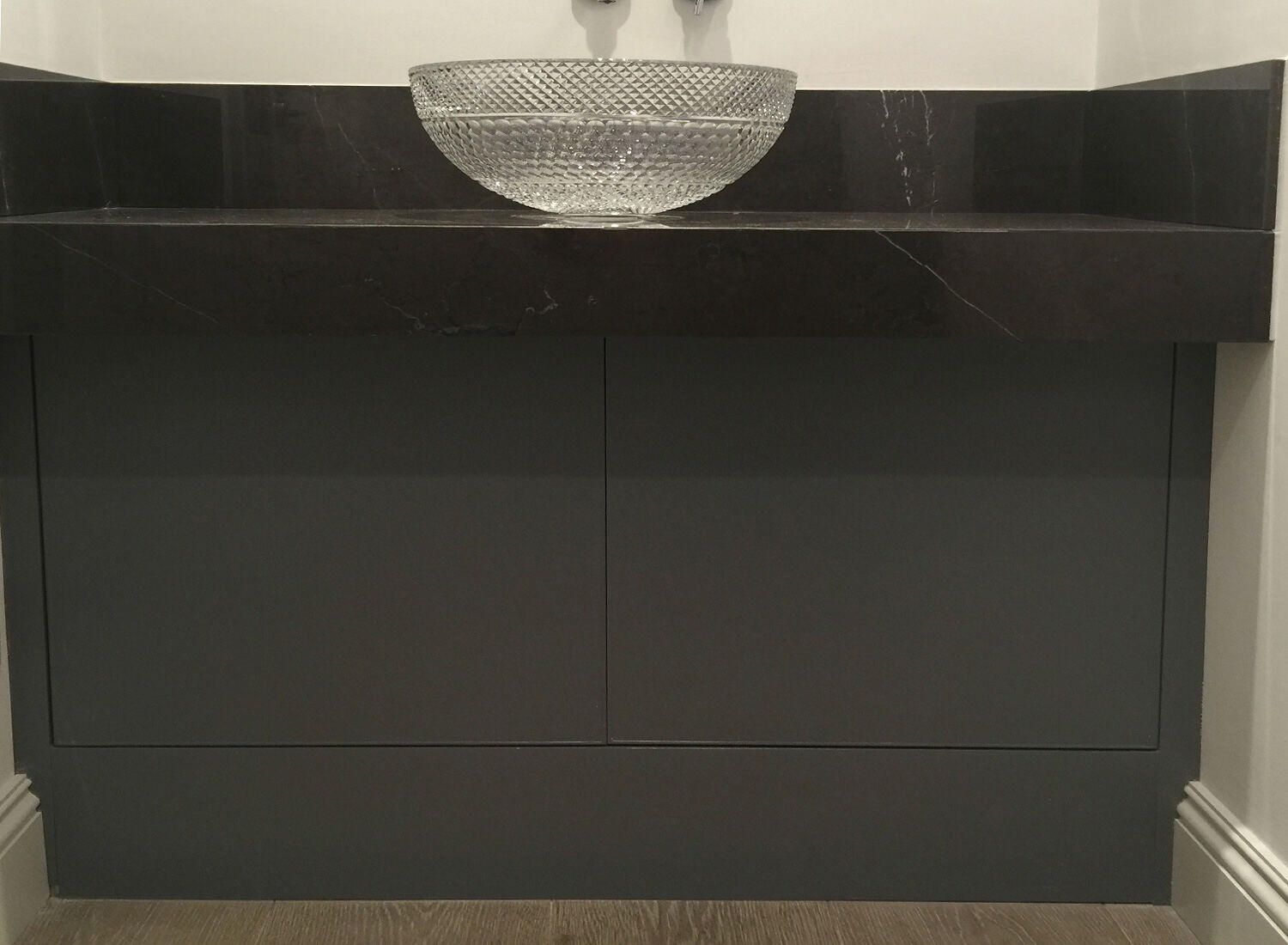 A made-to-measure vanity unit with a sprayed finish, a dark stone top and a cut-glass vessel basin